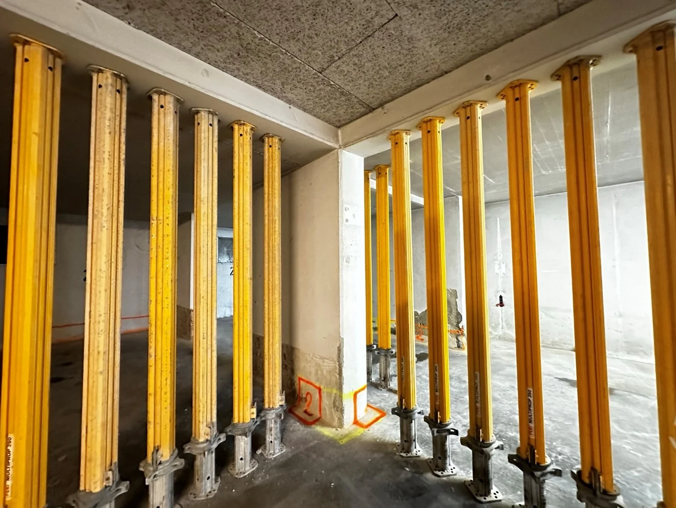 Reihe gelber Deckenstützen in einem Rohbau unter der Deckenschalung