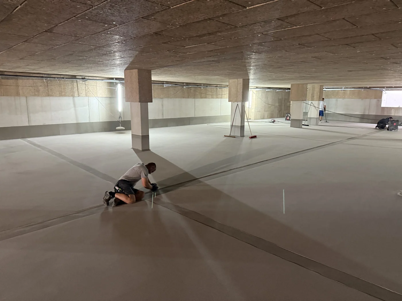 Weite, fertig beschichtete Tiefgarage mit hellem Boden, eine Person kniet prüfend an der Fläche.