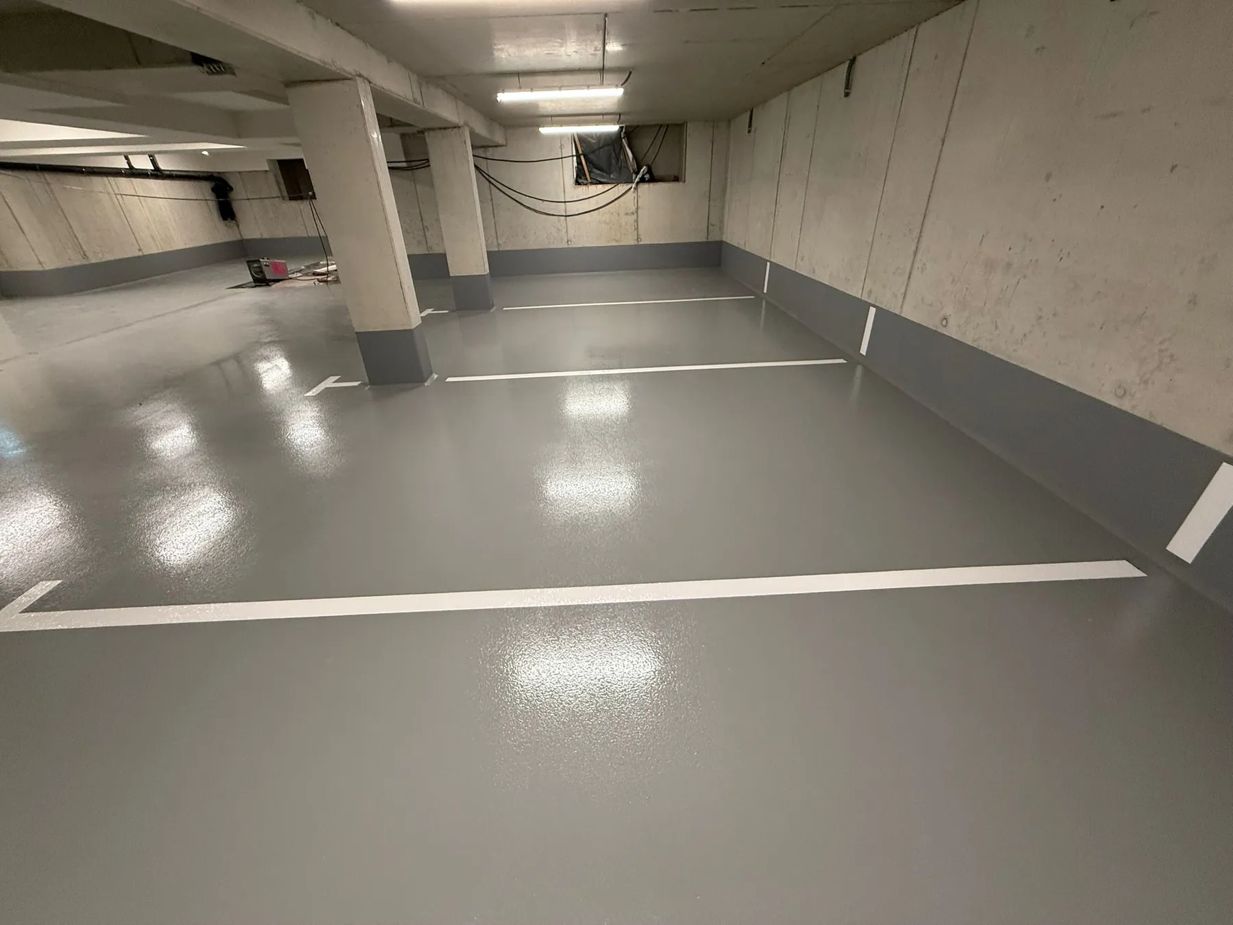 Fertige Tiefgarage mit glänzender grauer Bodenbeschichtung und Markierungen.
